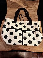 Full view of the Kate Spade canvas tote bag in cream with black polka dots, black handles, and front pockets.