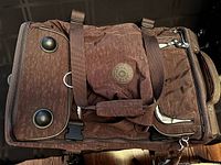 Top view of dark brown Kipling duffle bag showing the Kipling round logo patch, two black feet on the base, sturdy handles, and exterior zippered compartments.