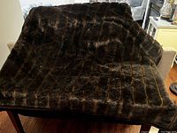 Full view of the dark brown faux fur throw blanket spread on a couch showing texture and size.