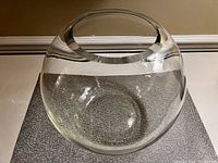 Top and side view of a large round clear crystal vase on a textured placemat, showing shape and opening.