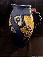 Side angle of blue pottery pitcher showing textured fish scale decorative elements and twisted handle with red nodules