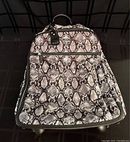 Front view of Tumi rolling carry-on bag showing snake print fabric exterior, zippered front pocket, and top handle with Tumi luggage tag.