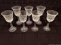 Seven Waterford crystal white wine glasses arranged in two rows on a black checkered cloth surface, showing clear cut crystal design and starburst base.