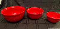 Set of three red ceramic mixing bowls with textured outer surface, staged side by side on black background.