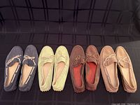 Photo showing four pairs of women's Cole Haan loafers in different colors laid side by side on a black checkered background.
