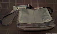 Full view of OGIO black leather and fabric messenger bag with shoulder strap on dark surface