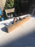 Side view of a long antique wooden carpentry plane with handle and blade visible, placed on white cloth outdoors