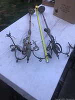 Pair of brass gaslight chandeliers laid out on a white cloth, showing overall size with measuring tape.