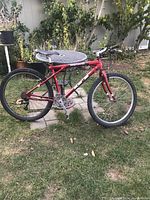 Side profile of the red GT mountain bike leaning next to a table in a yard, showing frame, tires, saddle and drivetrain.