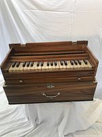 Front view of vintage Indian Bina harmonium showing keyboard and wooden casing with surface scratches and wear.