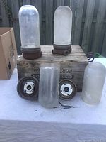 Five glass shades and two rusted metal light bases on wooden box, showing condition and components.