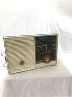 Front and side view of the turquoise and cream Philco clock radio with clock face and speaker grille.
