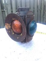 Front and side view of rusty metal lantern showing red and blue glass lenses with rust patches.