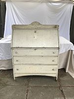 Front view of white painted vintage secretary desk with closed drop-front and three lower drawers.
