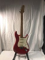Full front view of red Stratocaster-style guitar on stand against white backdrop