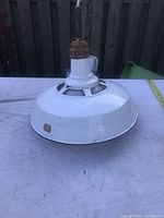 Vintage industrial light fixture with white enamel shade and some rust on top hardware, photographed on flat surface outside.