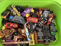 Wide shot showing many Disney Cars characters including Lightning McQueen, Mater, and others stacked loosely in a green bin.