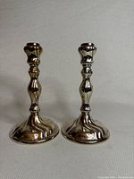 Photo showing the pair of silver candle sticks with ornate sculpted design and polished finish on a fabric background.