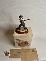 Figurine of a young baseball player batting stance on top of original box with certificates and tags.