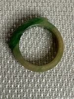 Close-up photo of an old jade ring showing a natural color gradient from green to light brown. The ring is solid and smoothly polished.