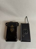 Old Zeiss Iconette folding camera next to black worn leather carrying case on beige fabric background