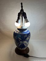 Front view of the lamp showing the porcelain vase with blue floral and leaf motifs under lighting, including the lamp hardware and bulbs.