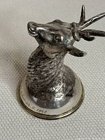 Angled front right view showing stag head tilt, textured fur and circular base with inscribed date.