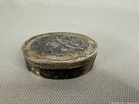 Overall front view of oval box resting on grey textile