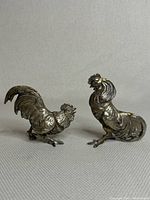 Pair of antique brass rooster figurines shown together on a neutral background to capture scale and condition.