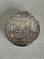 Top view of the oval trinket box showing detailed raised cherub design and ornate border.