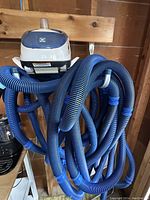 Hayward Navigator V-Flex vacuum head with attached coiled blue hoses hanging on a hook against wooden wall