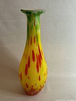 Front view of large art glass vase with bright yellow base, red streaks and green rim, showing shape and color pattern