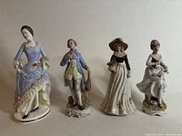 Four ceramic figurines side by side on a neutral background showing variety in dress and posture