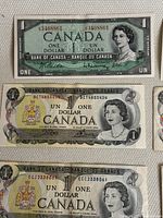 Photo showing three vintage Canadian one dollar bills with different designs and serial numbers, featuring Queen Elizabeth II