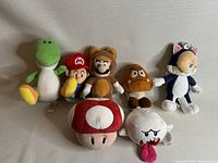 Front view of all seven Mario World plush characters grouped together on a neutral background.