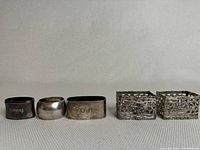 Five assorted vintage napkin rings lined up showing different shapes and engravings.