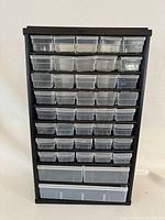 Front view of black plastic storage cubby organizer with multiple rows of clear plastic drawers arranged by size.