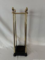 Full view of vintage umbrella stand showing four polished brass rods with pointed finials and a black cast iron base.