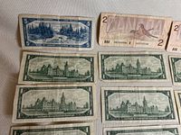 Photo of one $5 bill and multiple $1 bills showing the back side featuring Canadian Parliament building and front landscapes.