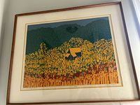 Framed serigraph print depicting barn in stylized field with mountains