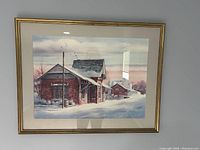 Framed watercolor painting showing a snowy scene with a large brick building, smaller buildings in the background, birds flying, and a colorful sky.