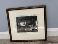Photo of framed black and white sketch showing chair by window, with visible reflection on glass and wall background.