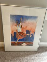 Full view of framed artwork showing a dancing lady in a red skirt and white blouse, city skyline in background, with matting and silver frame.