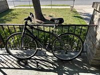 Side view of a black hybrid bike leaning against a metal railing outside, showing the entire bike including the frame, tires, and seat.