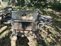 Outdoor barrel-style metal grill with wheels and thermometer on lid, showing rust and wear.
