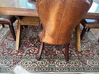 Photo shows area rug under a wooden dining table and leather chair, highlighting pattern and color details.