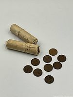 Two sealed paper rolls labeled “50 Pennies” accompanied by 10 loose Indian Head pennies laid out on white background