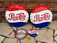 Four vintage advertising pressed tin buttons arranged outside against brick: two large Pepsi-Cola bottle cap style buttons, one smaller Pepsi-Cola button, and one Heinz Pickle button.