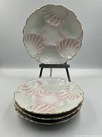 Stack of four pastel shell-shaped oyster plates with one displayed upright on a stand