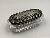 Closed view of the trinket container showing the antique sterling silver lid with hallmark and clear faceted glass base.